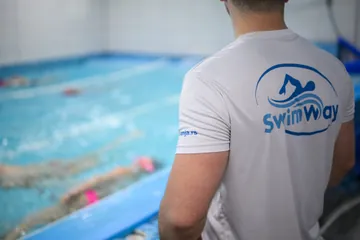 Trener u Swim Way majici prati polaznike sa ivice bazena