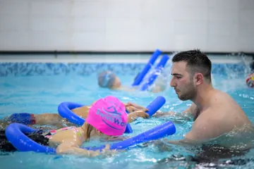 Trener pomaže detetu sa plivačkim valjkom u bazenu na Obilićevom vencu